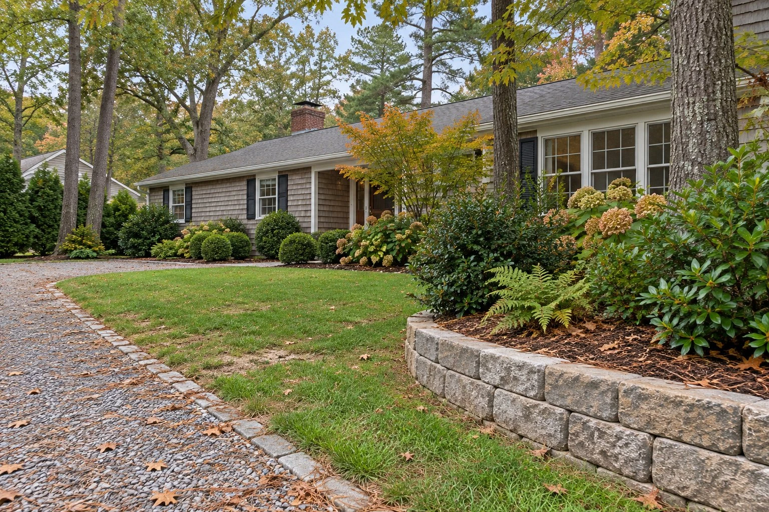 Cedar-shingled house among tall pines with a crushed-stone driveway and a bed of mountain laurel and ferns